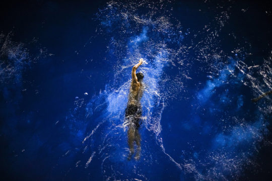 Image title: Soar in the blue There was a diving practice, after that, the swimming coach was swimming in the pool, and I was standing in the 5m diving platform, waiting for the right moment, although the light was quiet dim, I still managed to get this one.